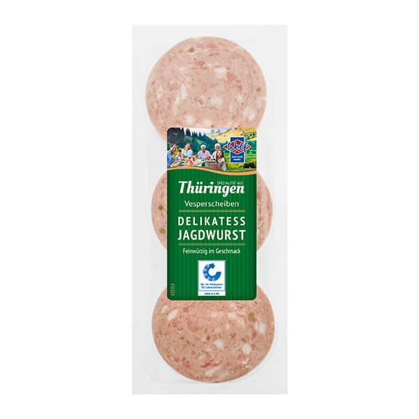 Das Wolfprodukt "Vesperscheiben Delikatess Jagdwurst" in einer durchsichtigen Verpackung. Auf dem Etikett ist eine Familie, die gerade Brotzeit macht. Eltern mit zwei Kinder und Großelter. Im Hintergrund sieht man grüne Landschaft.