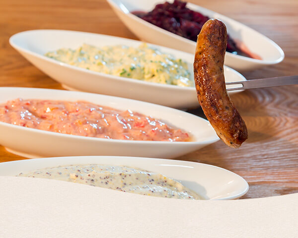 Eine gebratene Nürnberger Wurst mit vier verschiedenen Dip.