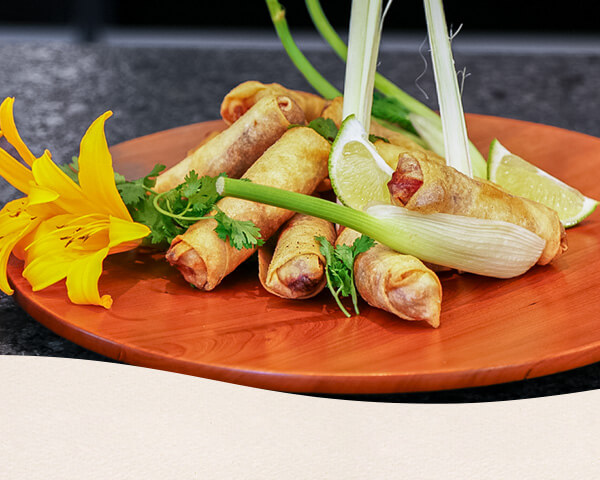 Die fertigen Frühlingsrollen wurden auf einen Teller gelegt, mit Blumen und Lauch dekoriert.