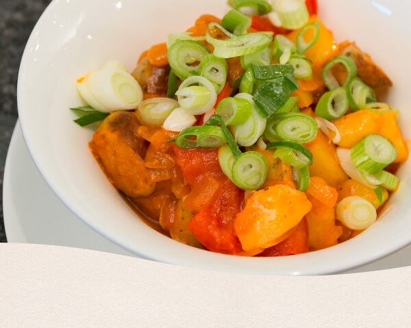 Gulasch aus Kartoffeln, Paprika, Zwiebel und Nürnberger Würstchen getoppt mit Frühlingszwiebel.