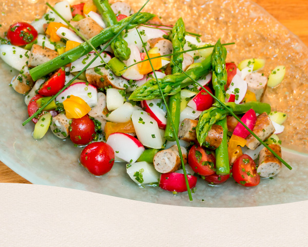 Foto von oben einer großen Servierplatte von dem Spargelsalat mit Radieschen, Karotten, Tomaten und Nürnberger Würstchen.