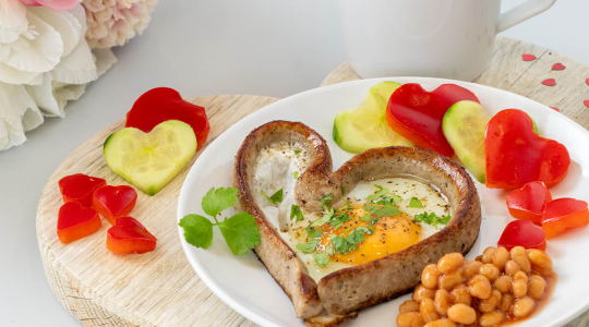 Frühstücksteller mit einem Bratwurstherz gefüllt mit Spiegelei. Dazu Gemüse in Herzform und Baked Beans