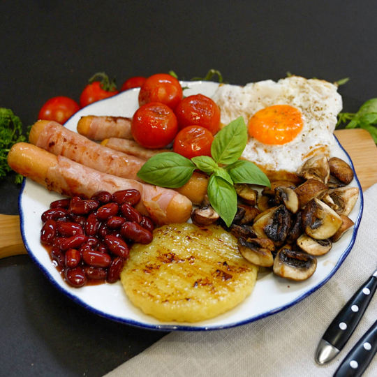 Englisches Frühstück mit Berner Würstchen, Roundies, Baked Beats, Champions, Tomaten und Spiegelei auf Toast