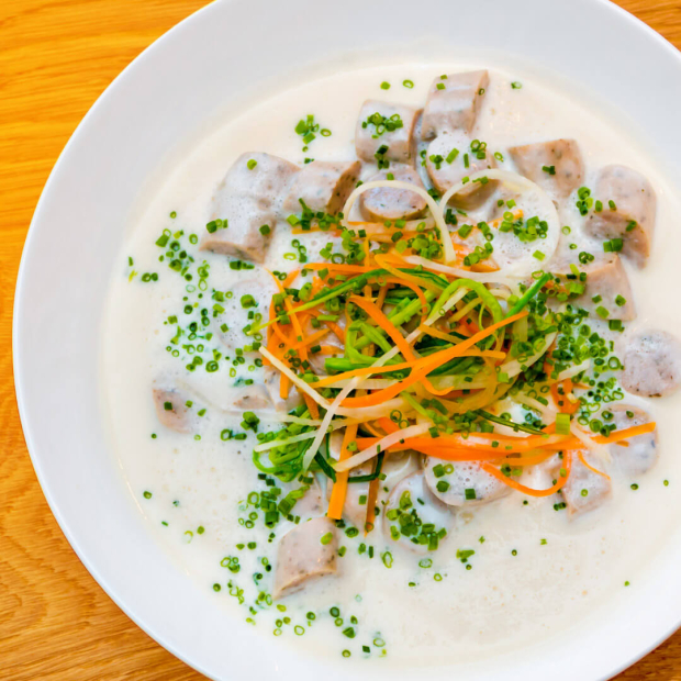 Nürnberger Würstchen in Stücken geschnitten in einem weißen Zwiebelsud mit Gemüsedeko.